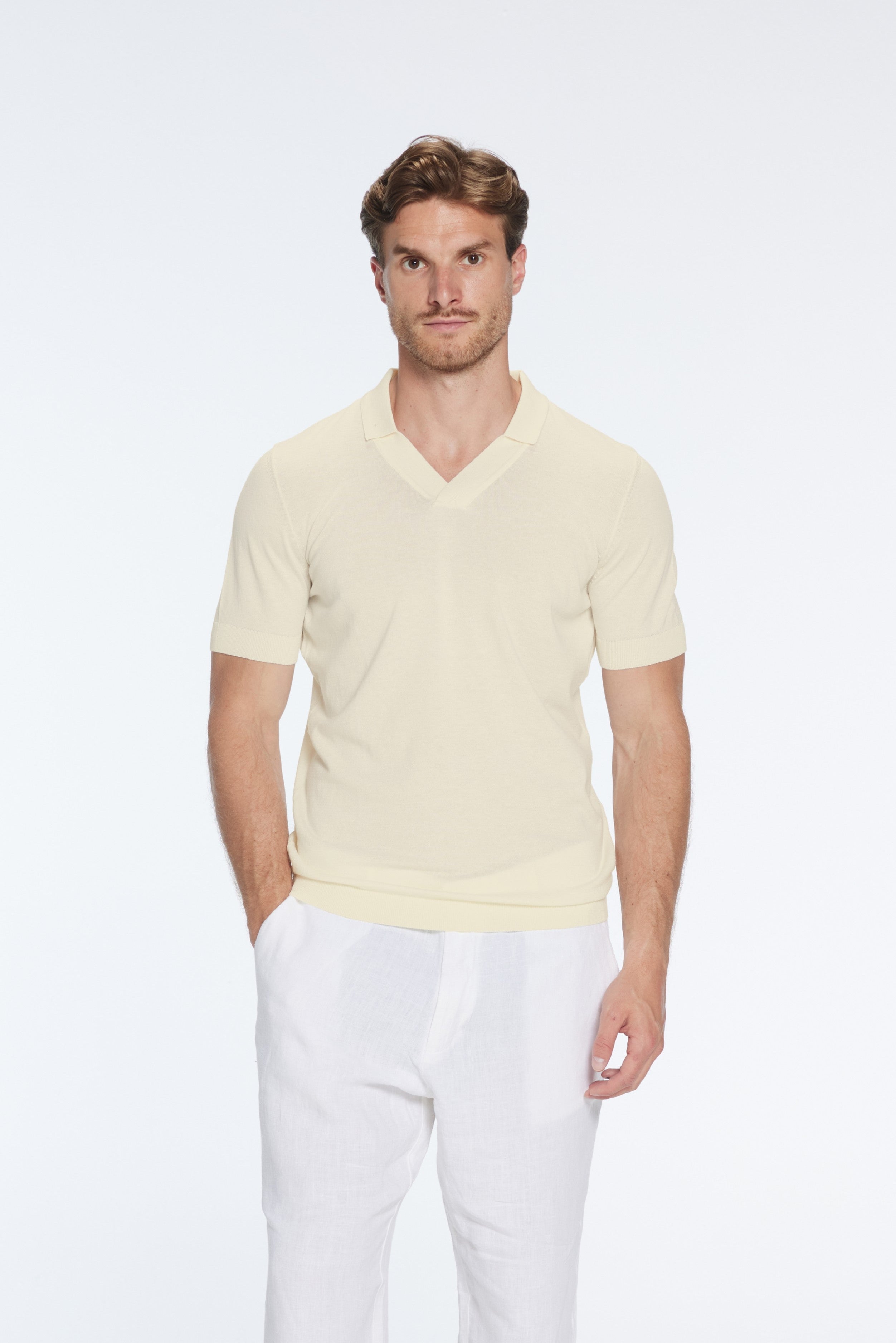Man wearing a light yellow V-neck sweater and white pants on a white background