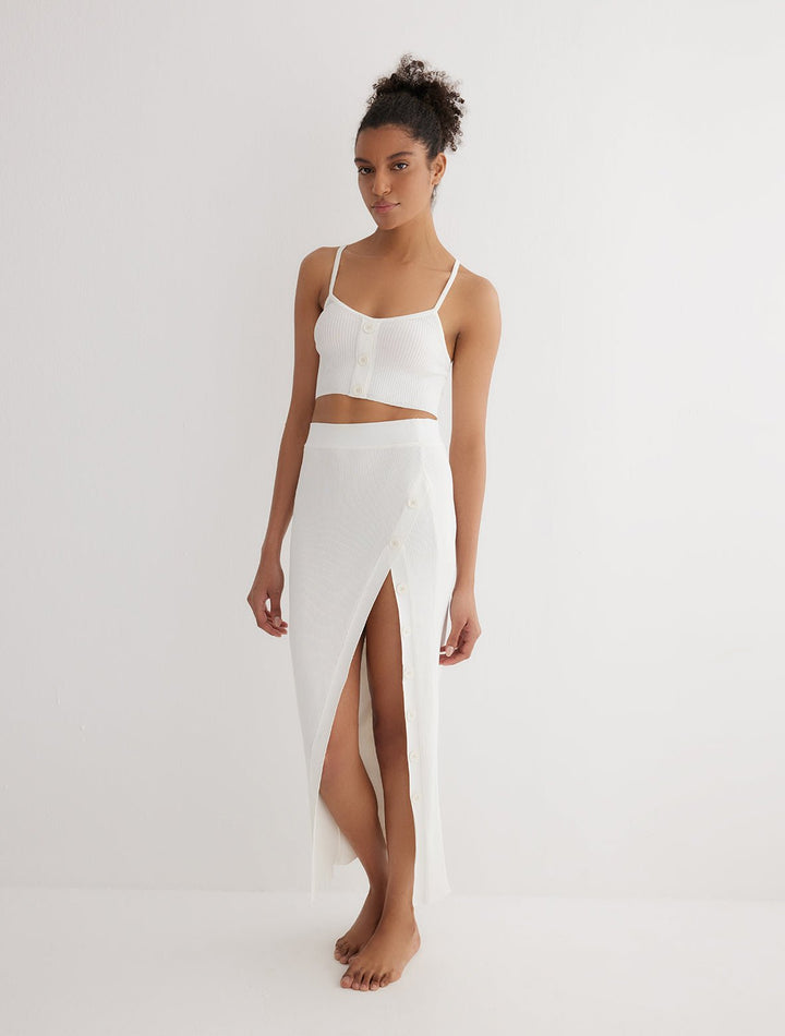 Front View: Model in Jules White Skirt - MOEVA Luxury Swimwear, Knitted Skirt, Button Detail Throughout, Side Assymmetrical Skirt, Elasticated Waistband, Front Slit, MOEVA Luxury Swimwear