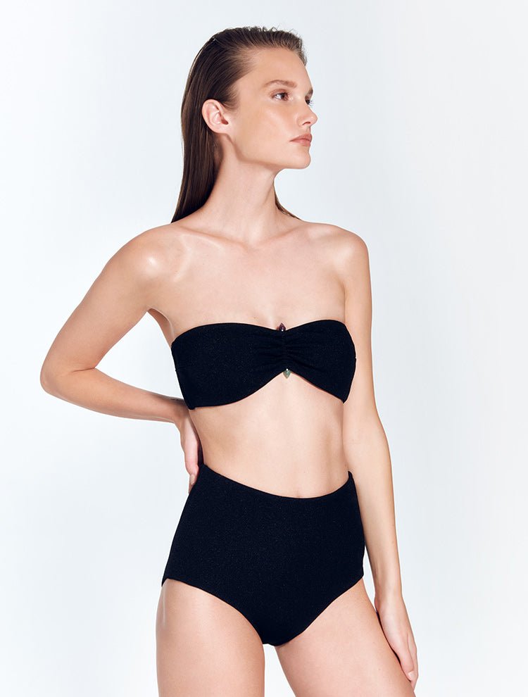Front View: Model in Zeta Shiny Black Bikini Top - MOEVA Luxury Swimwear, Italian Fabric, Strapless Bandeau Bikini Top, Strapless Top, Ruched Detailing, Amethyst & Aventurine Stones Accessory, Removable Paddings, MOEVA Luxury Swimwear