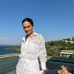 "Model wearing the Nayeli White Dress from the front, showcasing the broderie anglaise fabric, button front, and self-tie waist."