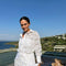 "Model wearing the Nayeli White Dress from the front, showcasing the broderie anglaise fabric, button front, and self-tie waist."