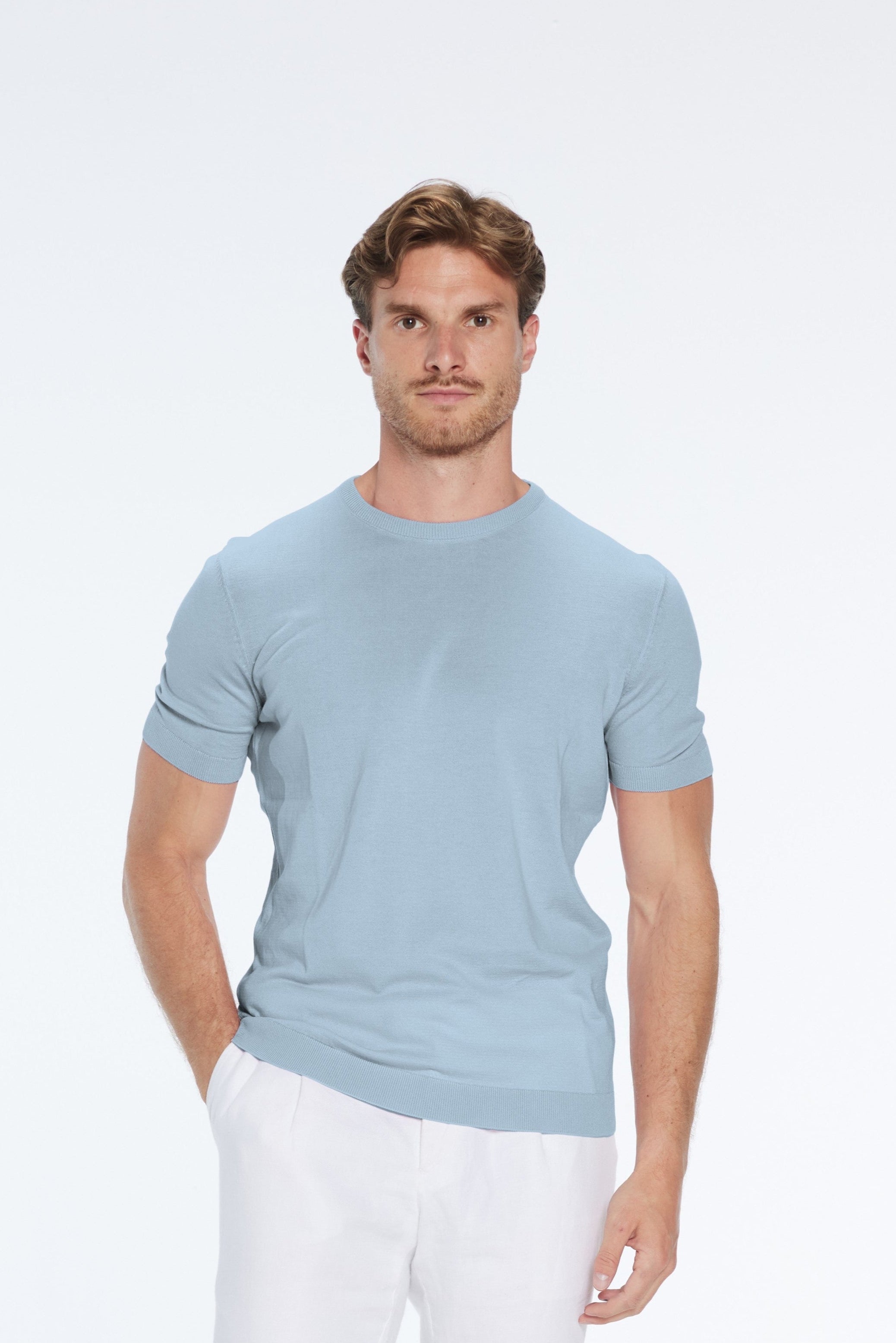 Man wearing a light blue shirt and white pants on a white background