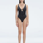 "Model wearing the Emma Black Underwired Swimsuit with a ruched front and moderate bottom coverage, standing poolside."
