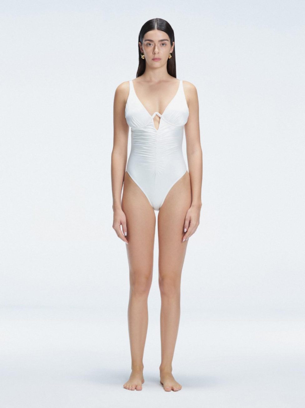 "Model wearing the Emma White Underwired Swimsuit with a ruched front and moderate bottom coverage, standing poolside."
