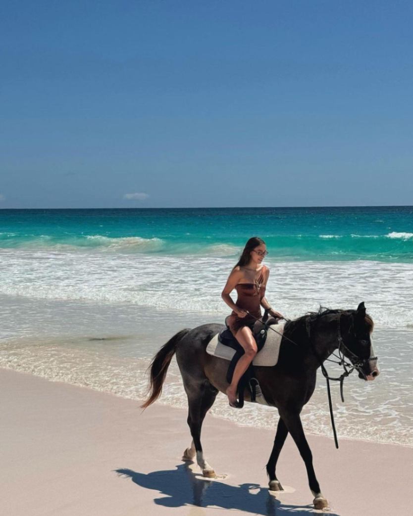 Veronia Jankovska wearing the Halin Brown Swimsuit, showcasing its one-shoulder design and gold sculpted accessory.
