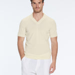 Man wearing a light yellow V-neck sweater and white pants on a white background