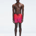 Model wearing Griffin Red Gradient Swim Shorts with pink-red print and sporty piping.