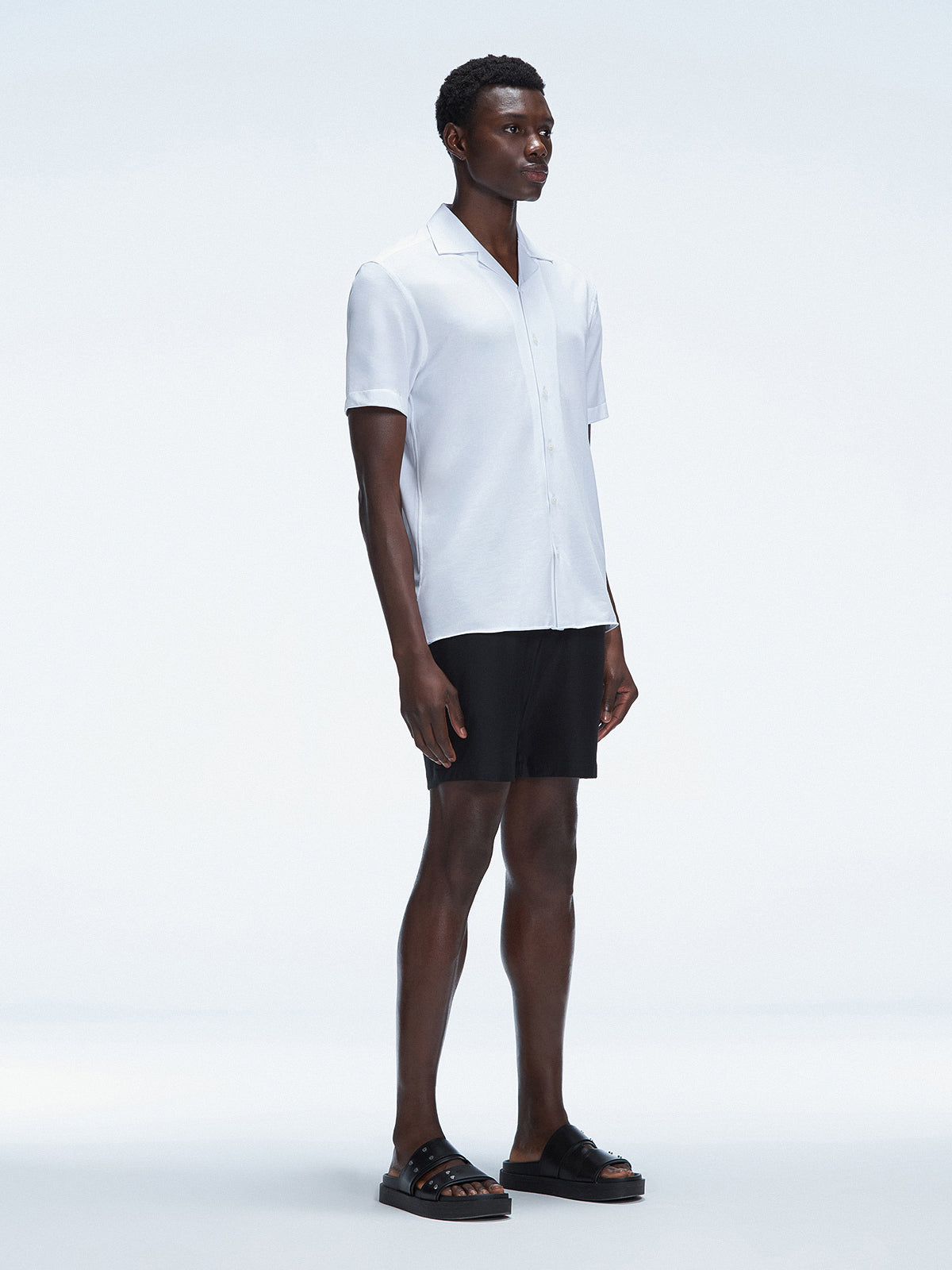Side  view of the Atticus White Polo T-Shirt on a model, highlighting the sleek open collar and short sleeves.
