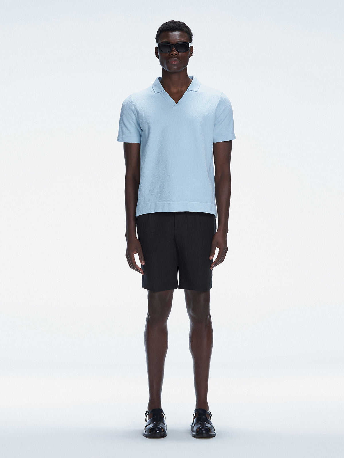 Model wearing Atticus Baby Blue Polo T-Shirt with open collar and slim fit, standing casually in a park.
