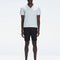 Model wearing Atticus White Polo T-Shirt with open collar and slim fit, standing in a relaxed outdoor setting.

