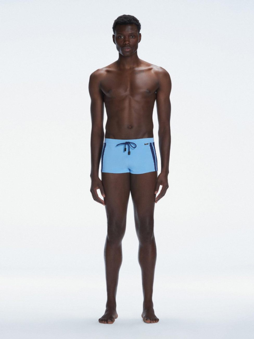 Model wearing Antonio Baby Blue/Blue Swim Trunks with a tight, form-fitting design.

