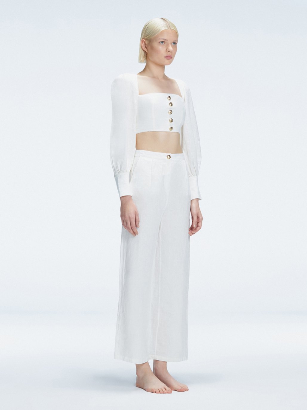 Side view of model showcasing the crisscross back detail on the Gemma White Cropped Top and Valencia White Pants.
