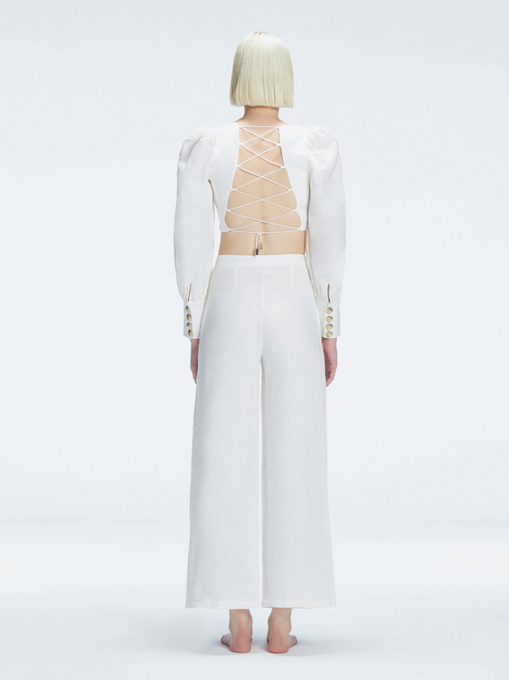 Back view of model wearing Valencia White Pants, highlighting the crisscross back straps and high-waisted fit.
