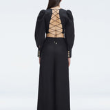 Back view of model wearing Gemma Black Cropped Top and Valencia Black Pants, highlighting the bold crisscross back design.
