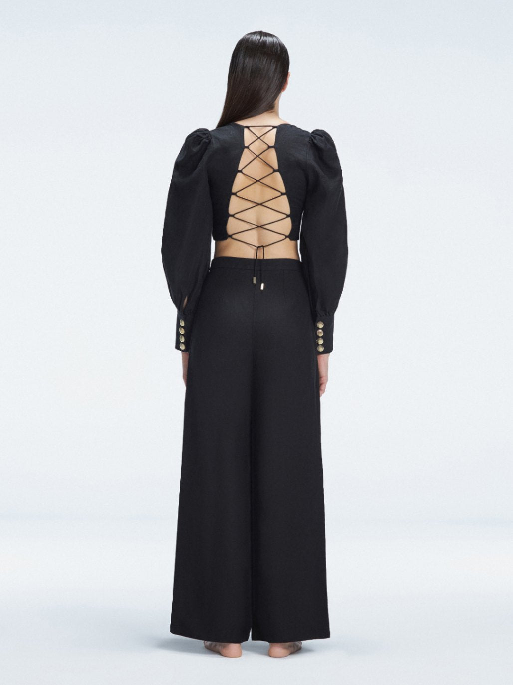 Back view of model wearing Gemma Black Cropped Top and Valencia Black Pants, highlighting the bold crisscross back design.
