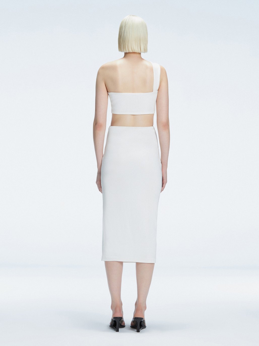 Back view of model wearing Lane White Top, highlighting the sleek one-shoulder silhouette.
