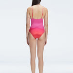 Back view of model wearing Marina Degraded Red-Pink One Piece swimsuit, featuring accessory details on straps and open back design.
