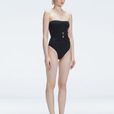 Side view of model showcasing the strapless design and gold accent on the Ursula Black One Piece swimsuit.
