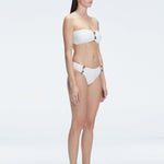 "Model in the Ilana White Bikini Set viewed from the side, highlighting the stylish buckle detail and ruched accents."

