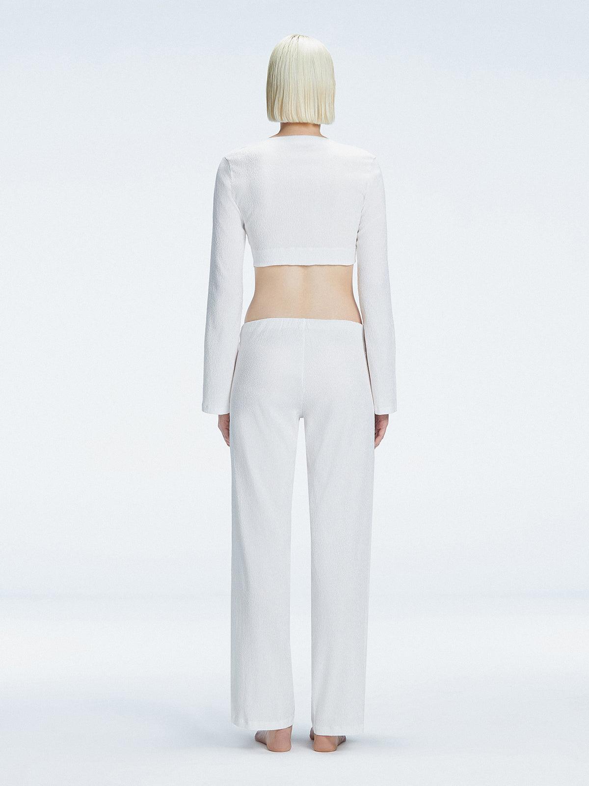 Back view of model wearing Sirenia White Crop Top and Helena Pants, highlighting the mid-rise V-shaped waistline and wide-leg design.
