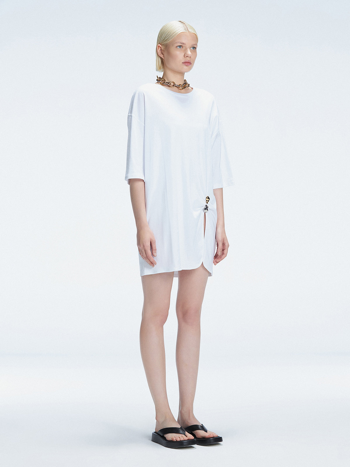 Side view of model showcasing the oversized fit and slit detail on the Lavinia White Dress.
