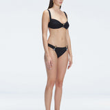 Side view of model showcasing the Emilia Black Bikini Top's adjustable straps and bold buckle design.
