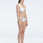 Side view of model showcasing the Emilia White Bikini Top's adjustable straps and bold buckle design.
