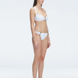 Side view of model showcasing the Emilia White Bikini Top's adjustable straps and bold buckle design.
