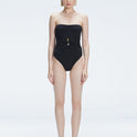 Front view of model wearing Ursula Black One Piece swimsuit with strapless silhouette and twisted gold accessory.
