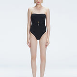 Front view of model wearing Ursula Black One Piece swimsuit with strapless silhouette and twisted gold accessory.
