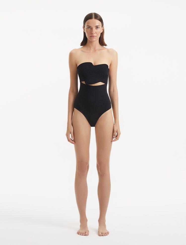 Model in front pose wearing Adria Black Swimsuit with wavy texture, underwire support, and adjustable straps. The swimsuit features a deep V neckline and full bottom coverage, crafted from premium Italian fabric.