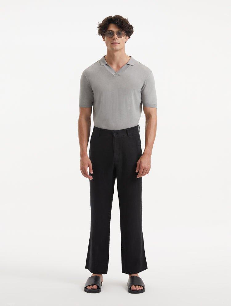 Model wearing Adrian Black Pants from the front, showcasing the relaxed fit and straight cut. The pants feature a mid-rise waist, button detailing, and practical welt pockets, paired with sleek dress shoes.