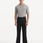 Model wearing Adrian Black Pants from the front, showcasing the relaxed fit and straight cut. The pants feature a mid-rise waist, button detailing, and practical welt pockets, paired with sleek dress shoes.