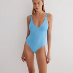 "Model wearing the Agneta Blue/Baby Blue reversible bodysuit from the front, showcasing its scoop neckline, long sleeves, and thong bottom. "