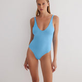 "Model wearing the Agneta Blue/Baby Blue reversible bodysuit from the front, showcasing its scoop neckline, long sleeves, and thong bottom. "