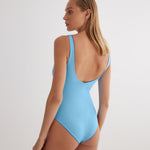 "Model wearing the Agneta Blue/Baby Blue reversible bodysuit from the back, highlighting its scoop neckline, long sleeves, and thong bottom."
