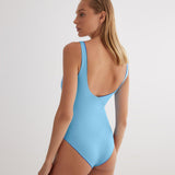 "Model wearing the Agneta Blue/Baby Blue reversible bodysuit from the back, highlighting its scoop neckline, long sleeves, and thong bottom."