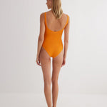 "Model wearing the Agneta Orange/Pink reversible bodysuit from the back, highlighting the thong bottom and seamless design. "