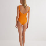 "Model wearing the Agneta Orange/Pink reversible bodysuit from the back, highlighting the thong bottom and seamless design. "