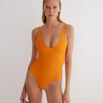 "Model wearing the Agneta Orange/Pink reversible bodysuit from the front, showcasing its modern design with a scoop neckline and body-hugging fit. "