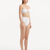 Model presenting the Baia White Bikini Set from the side, emphasizing the elegant silhouette of the bandeau top and the chic cut of the bikini bottom.