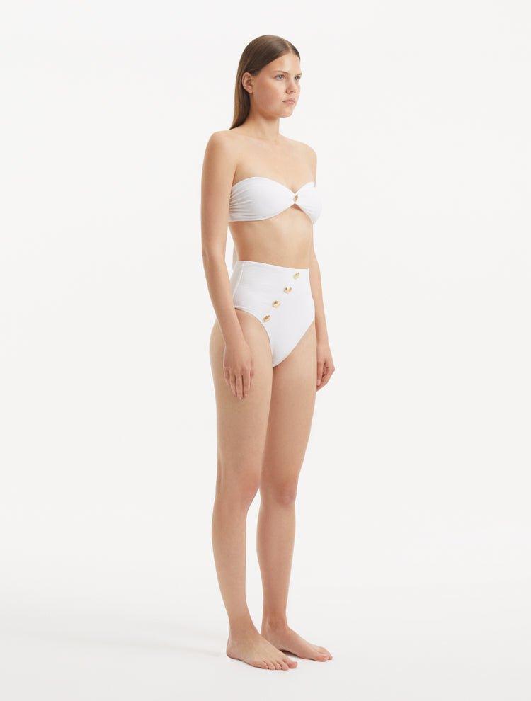 Model presenting the Baia White Bikini Set from the side, emphasizing the elegant silhouette of the bandeau top and the chic cut of the bikini bottom.