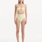 Model showcasing the Baia Yellow Bikini Set from the front, highlighting the sun-kissed bandeau top with gold shell buttons and the minimalist bikini bottom with gold detailing.