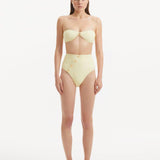 Model showcasing the Baia Yellow Bikini Set from the front, highlighting the sun-kissed bandeau top with gold shell buttons and the minimalist bikini bottom with gold detailing.