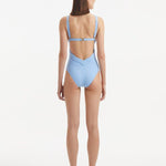 Back view of Breena Baby Blue Swimsuit, highlighting low-back cut and gold clasp detailing.