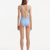 Back view of Breena Baby Blue Swimsuit, highlighting low-back cut and gold clasp detailing.