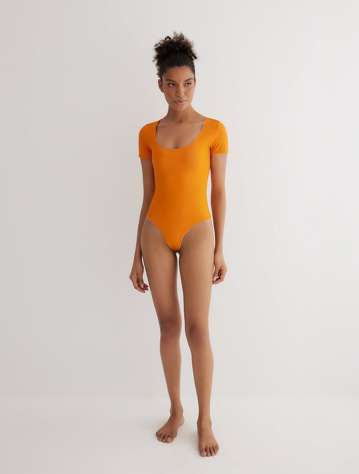 Front View: Model in Britt Orange/Pink Reversible Bodysuit - MOEVA Luxury Swimwear, 2 in 1 Reversible Bodysuit, UV Protection, Suitable for Swimming, Scoop Neckline, MOEVA Luxury Swimwear