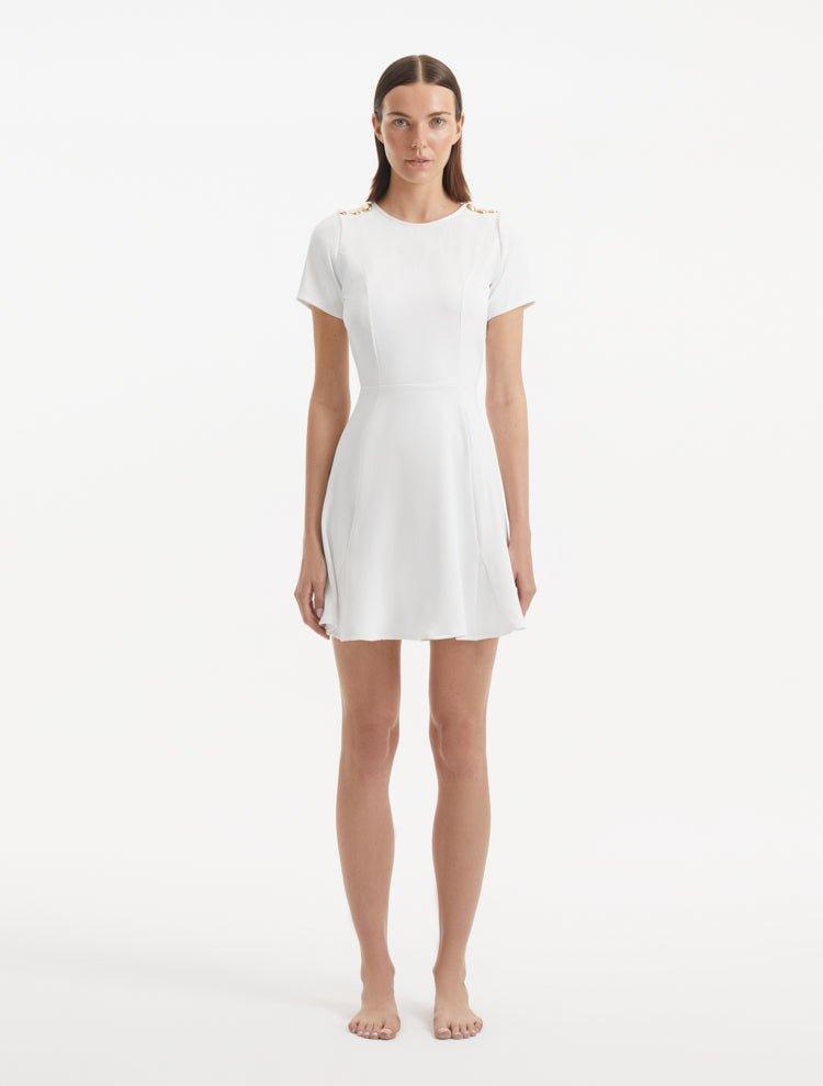 "Model wearing the Derin White Dress from the front, showcasing the knee-length cut, short sleeves, and shell-shaped gold buttons."