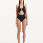 Model wearing the Dwyn Black Swimsuit, highlighting the tie-neck design and gold sculpted accessory.