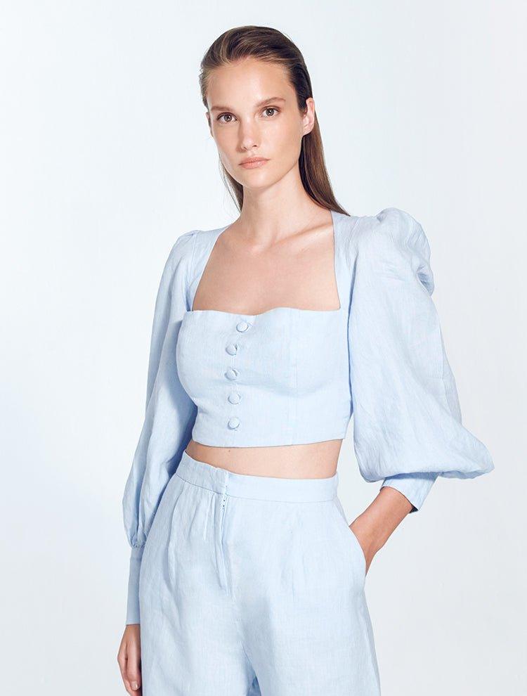 "Model wearing Eliana Baby Blue Top with square neckline, blouson sleeves, and adjustable lace-up back, paired with high-waisted pants"